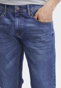 Mörkblå denimjeans med en klassisk passform. Funktioner inkluderar knappstängning, sidofickor och subtila blekningar för textur.