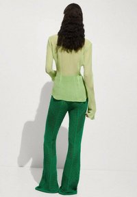 Pantaloni flared a maglia verde con motivo testurizzato abbinati a una blusa lunga a maniche lunghe verde chiaro e trasparente, che mette in risalto il design a strati e la trasparenza.