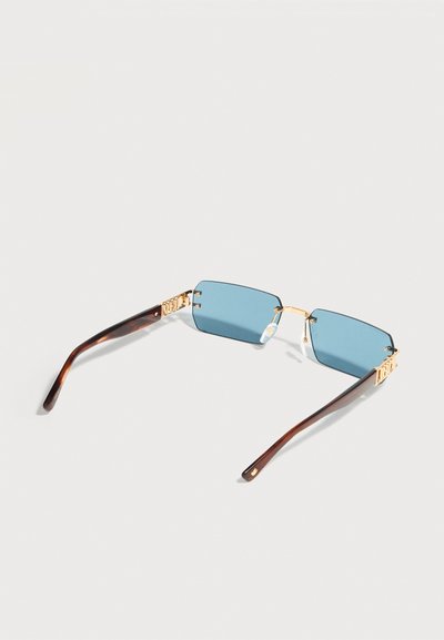 Μπλε ορθογώνια γυαλιά ηλίου με φακούς, με χρυσή μεταλλική γέφυρα και διακοσμητικά στοιχεία, σκούροι καμπυλωτοί βραχίονες σε σχέδιο χελώνας σε ανοιχτό φόντο.