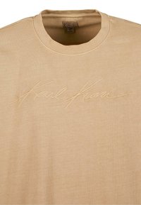 Šviesiai mėlynas megztinis su apykakle, pagamintas iš medvilnės, su siuvinėtu šviesiai beige „Karl Kani“ logotipu priekyje. Glotni tekstūra.