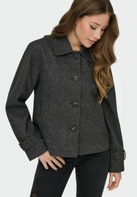 Sivý károvaný blazer s límcem, pěti černými knoflíky na zapínání a nastavitelné manžety. Materiál je strukturovaný a na tělo.