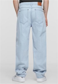 Hele sinine teksapüksid lahtise lõikega, viie taskuga ja tikandiga tagaküljel. Kombineeritud valgete jooksujalatsitega.