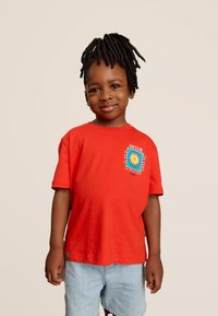 Rode katoenen t-shirt met korte mouwen, met een grafische print van een zon en tekst. Gecombineerd met lichtblauwe shorts, groene label aan de zoom.