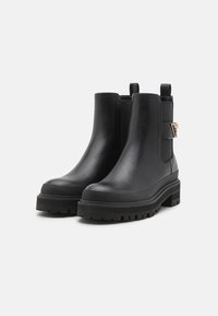 Botas de tobillo de cuero negro con suela gruesa, paneles laterales elásticos y detalle en hardware dorado en la correa. Suela antideslizante.