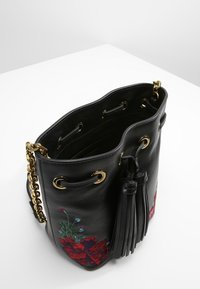 Svart läderhinkväska med guld detaljer, fransdetalj och blommig brodering i röd och blå på sidan. Öppen toppdesign med dragsnöre.