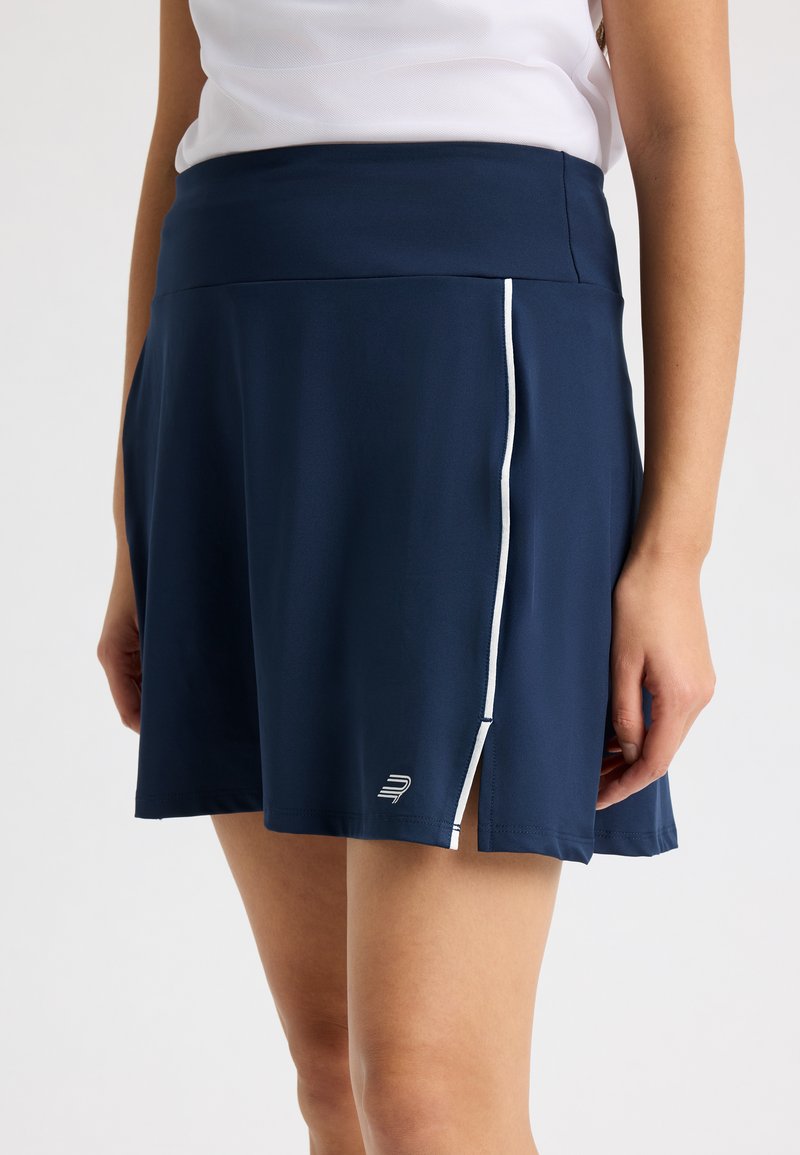 Falda deportiva azul marino confeccionada con una tela ligera, con una textura suave, ribete blanco en las costuras laterales y un logotipo bordado en el dobladillo.