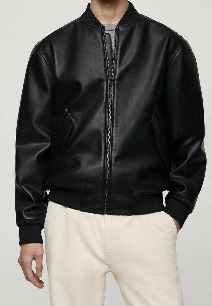 Homme portant une veste bomber en cuir noir avec fermeture éclair à l'avant et poignets côtelés, assortie à un pantalon de couleur claire, mains détendues le long du corps.