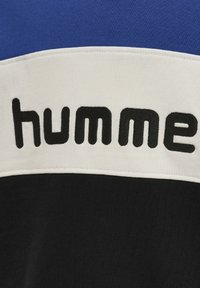 Czarna, biała i niebieska odzież sportowa z wyraźnym czarnym napisem "humme". Posiada design z blokami kolorów oraz gładką teksturę.