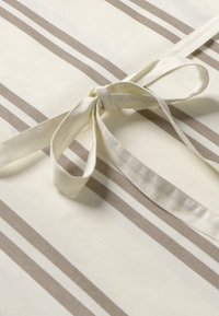 Tovaglia in cotone con sfondo crema e righe verticali marroni. Presenta una chiusura a farfalla realizzata con lo stesso tessuto.
