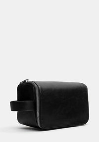 Borsa da toeletta rettangolare nera in pelle con una texture liscia. Presenta una chiusura con zip argentata e una maniglia laterale per facilitarne il trasporto.