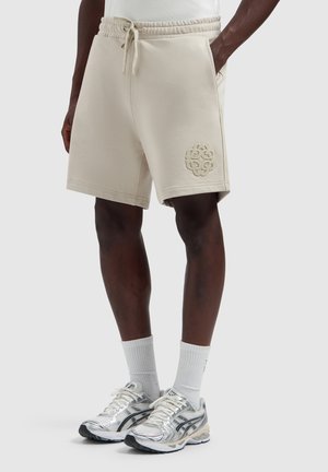 Person wearing beige drawstring shorts with side pockets and a textured logo, white ribbed socks, and silver running shoes.