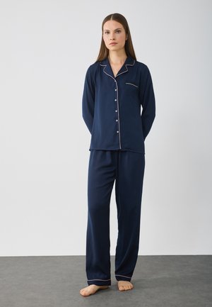 Set di pigiama navy in tessuto morbido caratterizzato da una camicia con bottoni e piping rosa, con maniche lunghe, abbinato a pantaloni larghi coordinati.