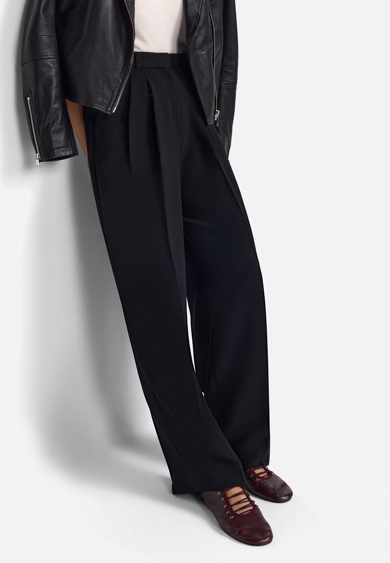 Pantalones negros de pliegues con cintura alta y diseño de pierna ancha, combinados con zapatos burdeos con cordones. Textura mate, con un ajuste relajado.
