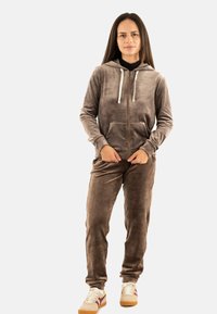 Felpa con zip in velluto marrone e pantaloni coordinati, con una tasca frontale, cappuccio regolabile e una texture liscia. Abbinati a sneakers.