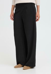 Pantalons larges noirs avec une texture lisse, présentés avec des plis sur le devant, une taille élastique et une coupe décontractée. Convient pour un usage décontracté.