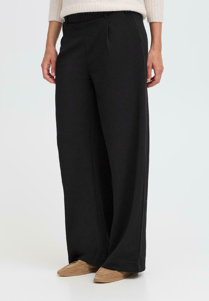 Pantalons larges noirs avec une texture lisse, présentés avec des plis sur le devant, une taille élastique et une coupe décontractée. Convient pour un usage décontracté.