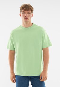 Jasnozielona bawełniana koszulka z okrągłym dekoltem, krótkim rękawem i luźnym krojem, zestawiona z niebieskimi dżinsami.