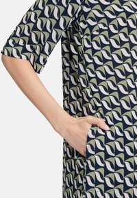 Abito blu navy con un motivo di forme verdi e bianche. Maniche corte e tasche laterali visibili con una vestibilità comoda.