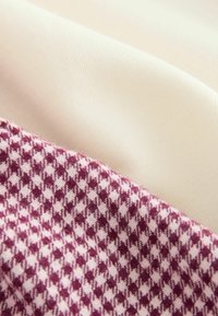 Wyeksponowane tekstylia: gładki kremowy materiał, teksturowany burgundowy i biały wzorzysty materiał z wzorem w kratę, nałożony pod kątem.