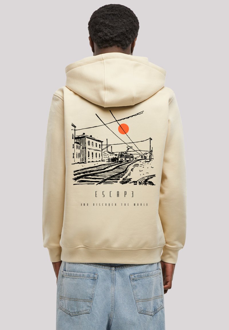 Person wearing a beige hoodie with a black sketch of train tracks, buildings, and a red sun, with text "ESCAPE" and "AND DISCOVER THE WORLD."