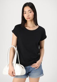 T-shirt noir à manches courtes avec col rond, associé à un short en denim et un sac à main blanc structuré avec de longues anses.