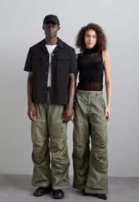 Unisex-Outerwear: ein schwarzes T-Shirt mit kurzen Ärmeln, grüne oversized Hosen mit Taschen und ein schwarzes ärmelloses Top. Glatte Stoffe und bequeme Passform.