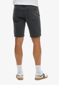 Shorts en denim gris avec un ourlet effiloché, poches arrière et coutures contrastantes, associés à des chaussettes blanches et des baskets noir et blanc.