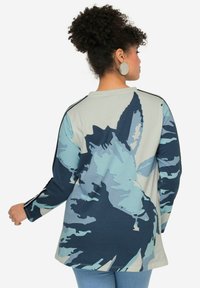 Camicia a maniche lunghe di colore azzurro chiaro con motivi astratti di foglie blu scuro, collo rotondo, vestibilità rilassata e strisce laterali sulle spalle.