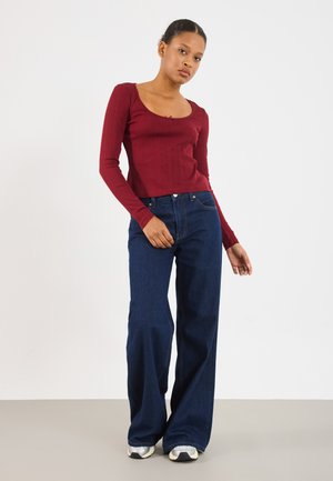 Un haut à manches longues rouge côtelé avec un col plongeant, associé à un jean large taille haute bleu foncé et des baskets grises.