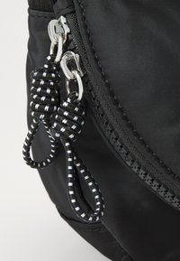 Black nylon bag with a zip closure featuring braided black and white zipper pulls and textured stitching along the zipper line.