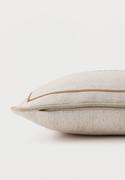 Coussin rectangulaire beige en tissu texturé avec un fin détail de bordure marron, présenté en profil latéral sur un fond blanc.