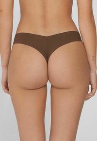 Brązowe, bezszwowe majtki typu thong o niskim stanie, gładkiej fakturze, minimalnym pokryciu i zaokrąglonym tylu dla wygodnego dopasowania.