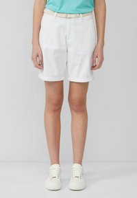Weiße Baumwollshorts mit aufgekrempelten Säumen, ausgestattet mit einem geflochtenen, hellen Gürtel. Kombiniert mit weißen lässigen Sneakern, vor einem neutralen Hintergrund.