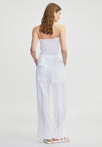 Witte, lichte, doorschijnende broek met verticale strepen en een elastische tailleband. Gecombineerd met een aansluitende witte tanktop en platte sandalen.