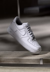 White leather sneaker with a perforated toe box, rounded laces, and a textured rubber sole. Features a visible Nike logo on the side.
