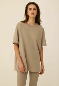 Beżowy, oversize'owy t-shirt z krótkimi rękawami, okrągłym dekoltem i gładką fakturą. Połączony z teksturowanymi beżowymi legginsami.