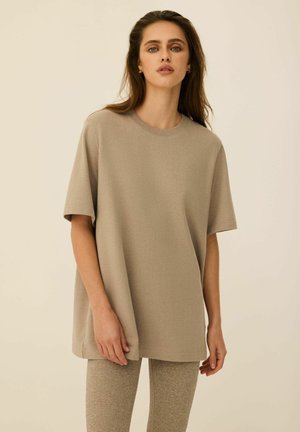 Beżowy, oversize'owy t-shirt z krótkimi rękawami, okrągłym dekoltem i gładką fakturą. Połączony z teksturowanymi beżowymi legginsami.