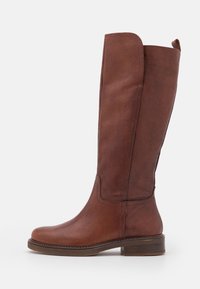 Botas de cuero marrón hasta la rodilla con punta redondeada, detalles de costura sutil y un tacón bajo y apilado. Textura suave con un ajuste a medida.