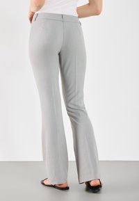Lichtgrijze uitlopende broek van een gladde stof, met een middelhoge taille, achterzakken en omgezoomde manchetten, gedragen met platte zwarte sandalen.