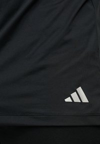 Κοντινή λήψη μαύρου υφάσματος με μικρό, λευκό λογότυπο Adidas στην κάτω δεξιά γωνία.