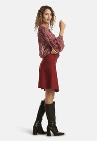 Red patterned blouse with voluminous sleeves paired with a fitted red skirt. Worn with knee-high black leather boots.