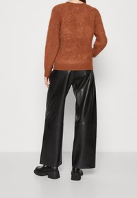 Rdzawoczerwony, puszysty sweter z prążkowanym dołem i mankietami, w połączeniu z czarnymi, skórzanymi spodniami o wysokim stanie i szerokimi nogawkami oraz masywnymi czarnymi botkami.