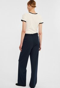 Witte korte mouwen top met zwarte afwerking, gecombineerd met marineblauwe gestreepte brede broek. Soepele textuur, aansluitende pasvorm en subtiel patroon.