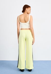 Light yellow wide-leg pants with black side stripes, paired with a fitted white crop top. Smooth texture with elastic waist.