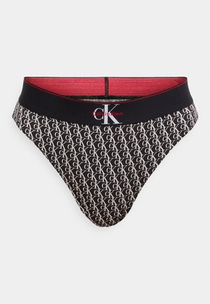 Črni tangice Calvin Klein s ponavljajočim vzorcem belega logotipa "CK", z enobarvnim črnim elastičnim pasom in rdečim poudarkom obrobe.