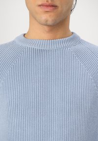 Pull en tricot bleu clair avec un col rond et un motif ribé texturé, doté de manches raglan.