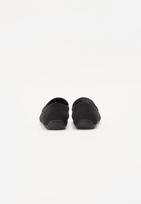 Sorte slip-on sko med en glatt semsket tekstur, avrundet bakdel og fleksibel gummisåle. Har diskrete røde detaljer på siden.