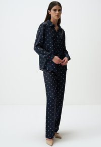 Navyblauw pyjama set van soepel materiaal met een herhalend licht patroon. Het shirt heeft een knoopsluiting en lange mouwen.