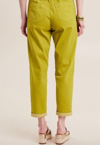 Groene cropped broek met opgerolde boorden, twee achterzakken en een gladde textuur, gecombineerd met tan platform sandalen.