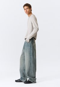 Ανοιχτό γκρι μακρυμάνικο πουκάμισο συνδυασμένο με φαρδιά ξεθωριασμένα μπλε τζιν. Το τζιν έχει άνετη εφαρμογή και μπροστινές τσέπες με ελάχιστες λεπτομέρειες ραφής.